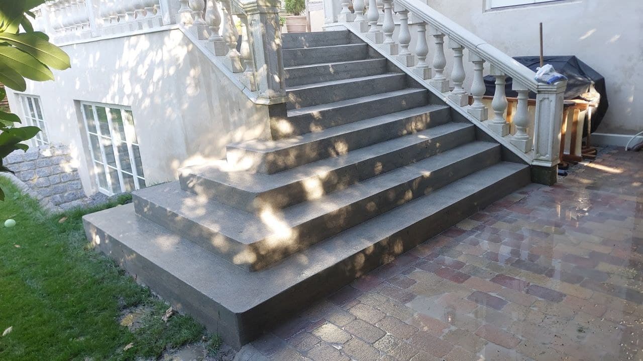 Nystøbt betontrappe med balustrade og naturstensbelægning ved villa
